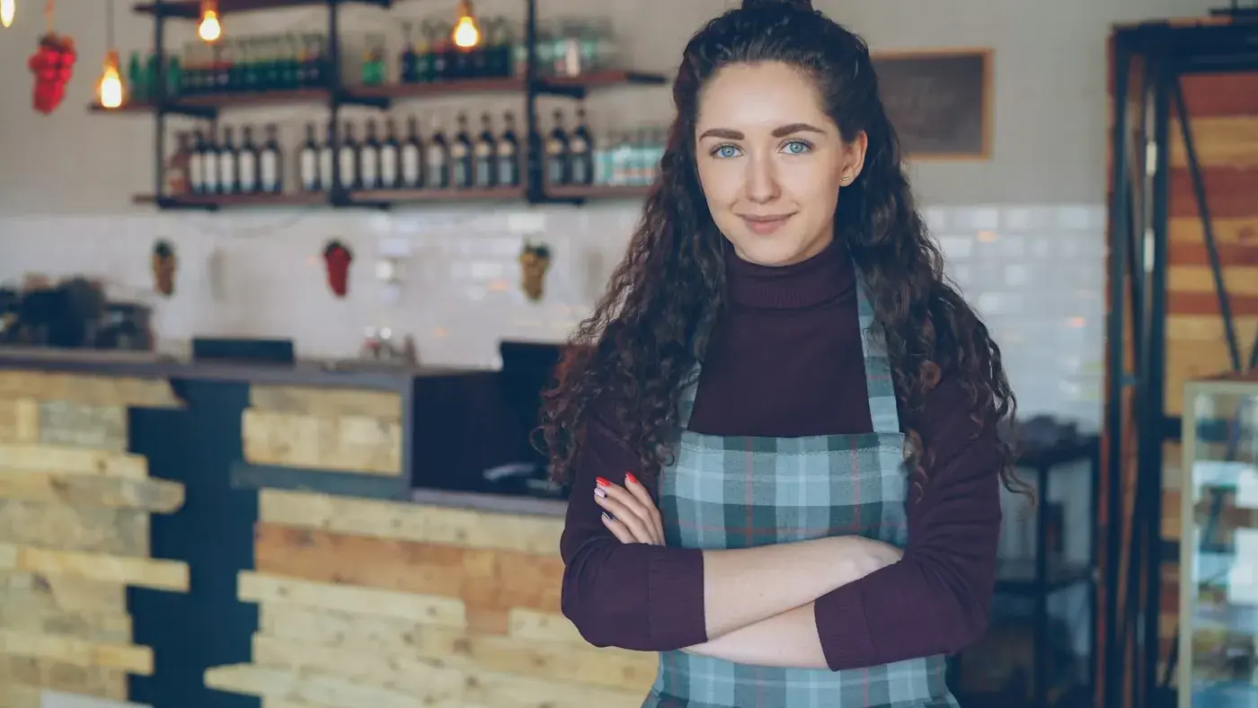 A café owner standing behind her counter with her arms folded