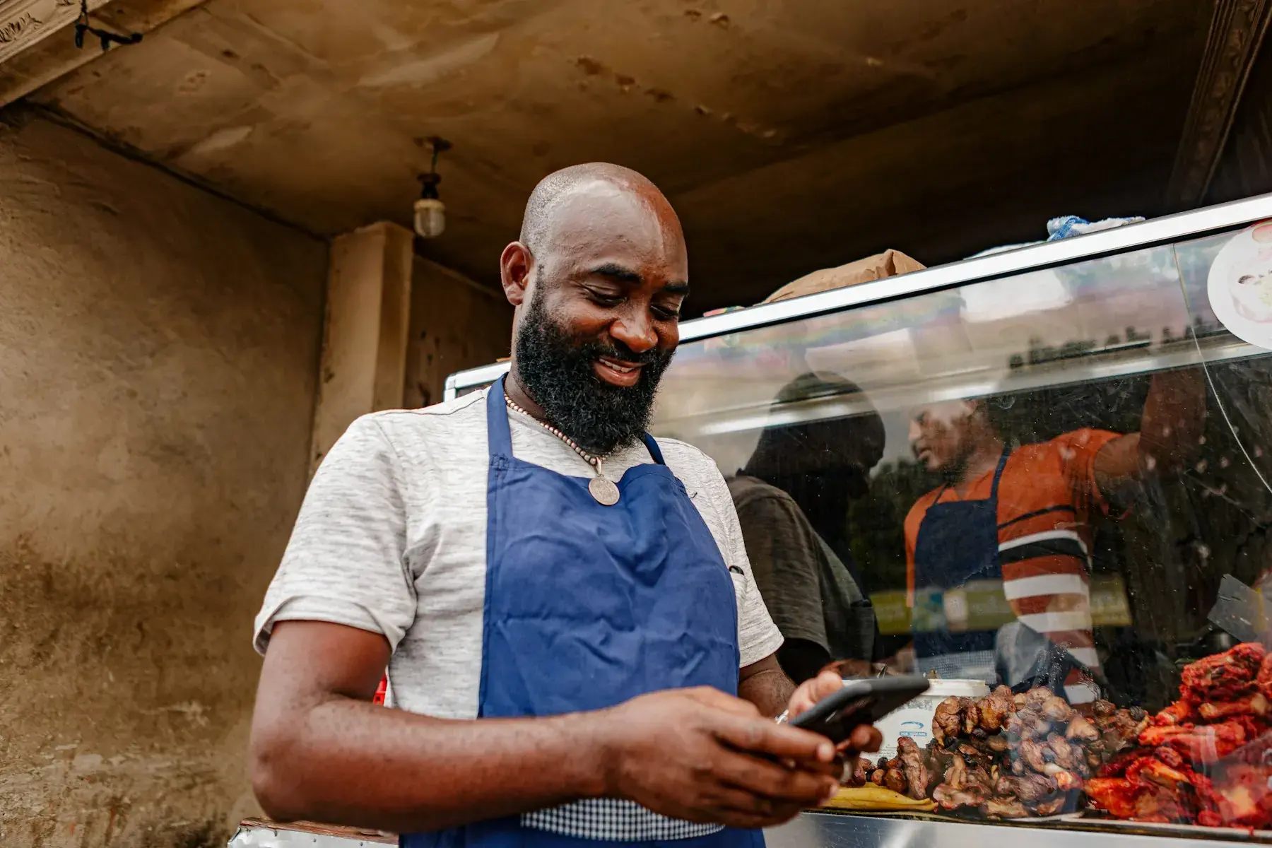 A business owner in an apron checking his phone at the counter of his shop
